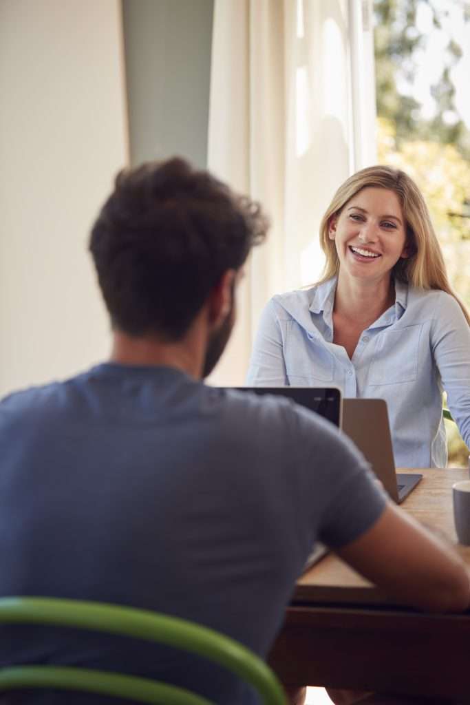 Couple With Laptop Sitting At Table Working From Home Together