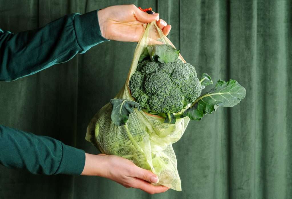 Male,Hand,Hold,Reusable,Bag,With,Broccoli,On,Green,Curtains